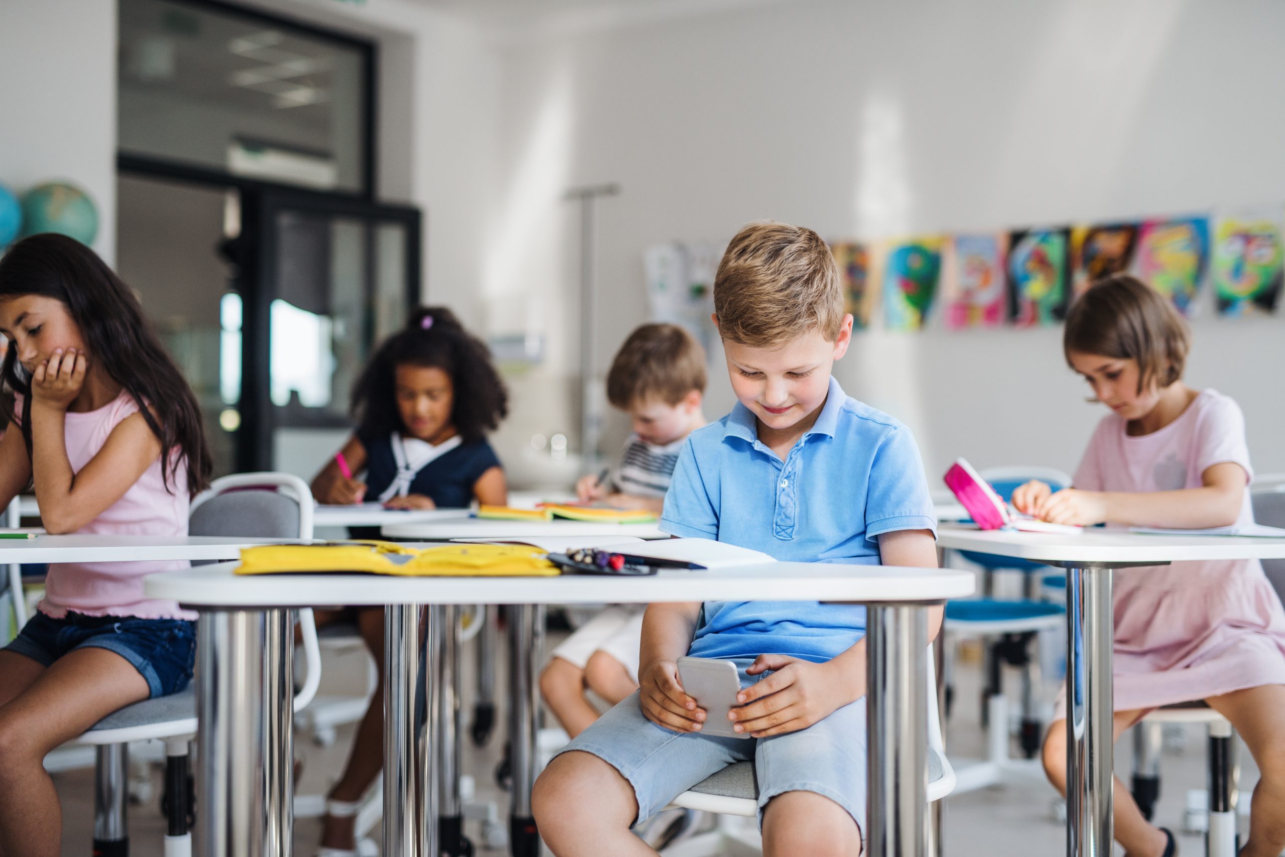 A,Small,School,Boy,With,Smartphone,Sitting,At,The,Desk